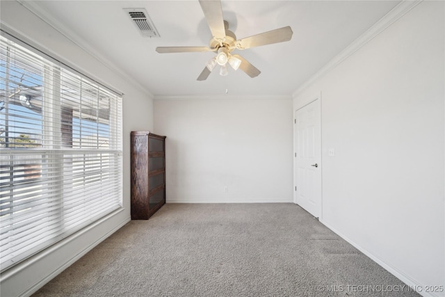 carpeted spare room featuring visible vents, baseboards, ornamental molding, and a ceiling fan