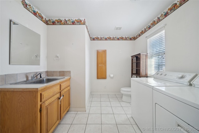 bathroom featuring tile patterned floors, toilet, a sink, washing machine and dryer, and baseboards