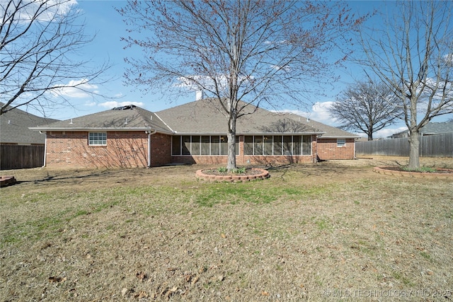 back of property featuring brick siding, a fenced backyard, a lawn, and a sunroom