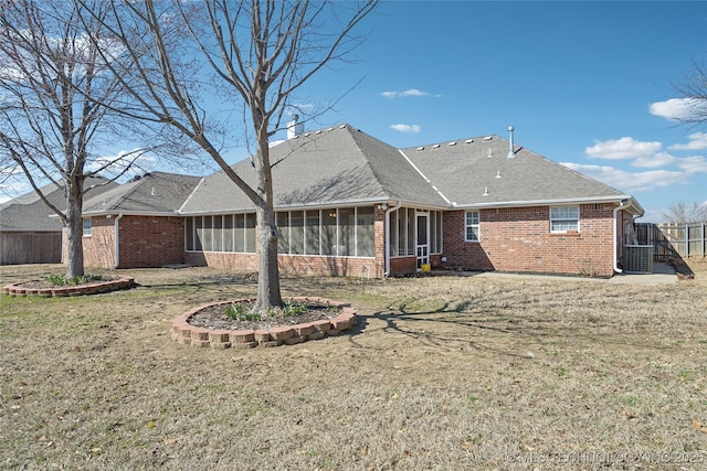 back of property featuring brick siding, fence, roof with shingles, a yard, and a sunroom