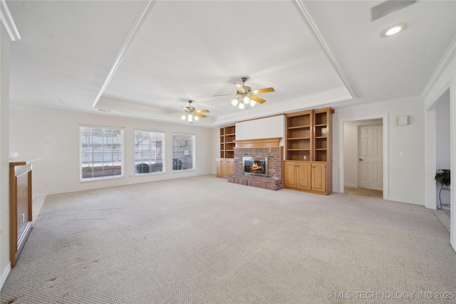 unfurnished living room with light carpet, ornamental molding, a ceiling fan, a tray ceiling, and a brick fireplace