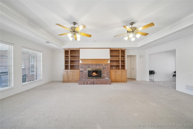 unfurnished living room with ceiling fan, a raised ceiling, ornamental molding, and light carpet