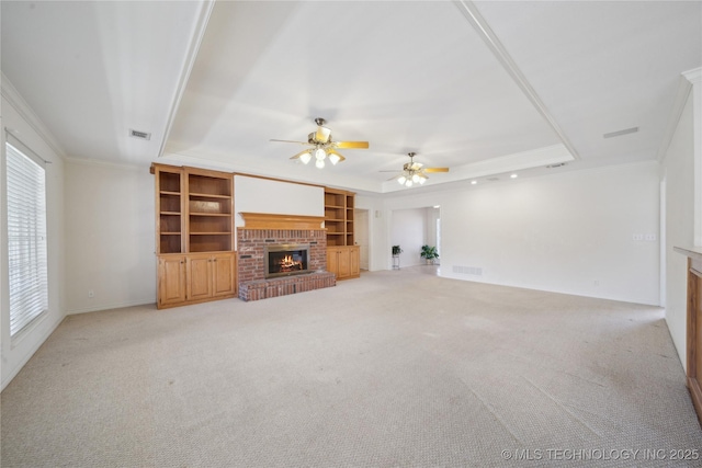 unfurnished living room with a tray ceiling, a brick fireplace, and ornamental molding