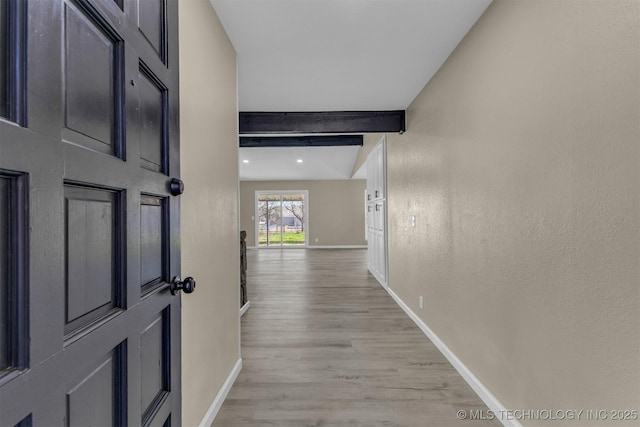 hallway with light wood-type flooring, baseboards, beamed ceiling, and a textured wall