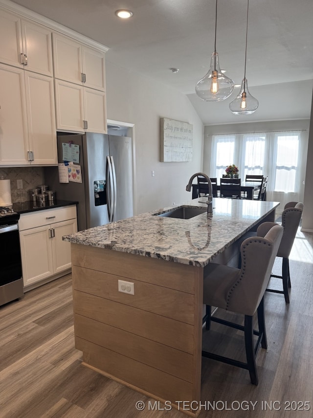 kitchen with a kitchen bar, a sink, wood finished floors, white cabinetry, and appliances with stainless steel finishes