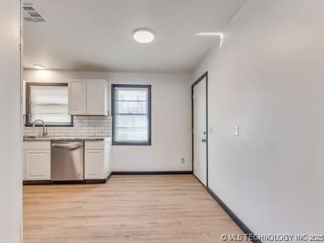 kitchen featuring light countertops, white cabinets, stainless steel dishwasher, light wood-type flooring, and backsplash