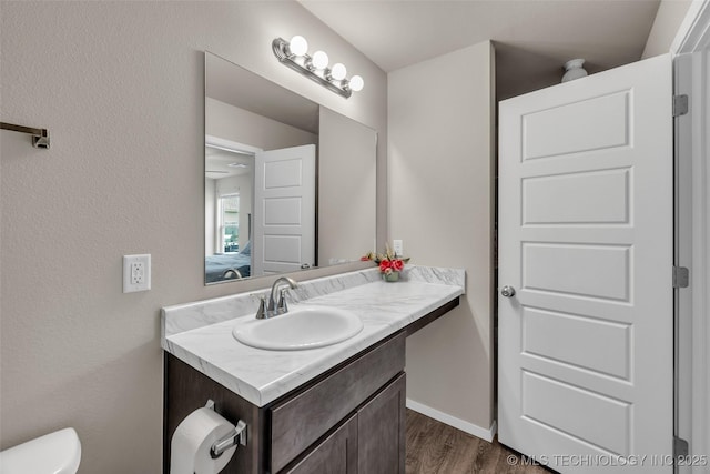 half bath with baseboards, toilet, wood finished floors, and vanity