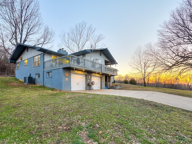 back of house at dusk with central AC, a yard, concrete driveway, a garage, and brick siding