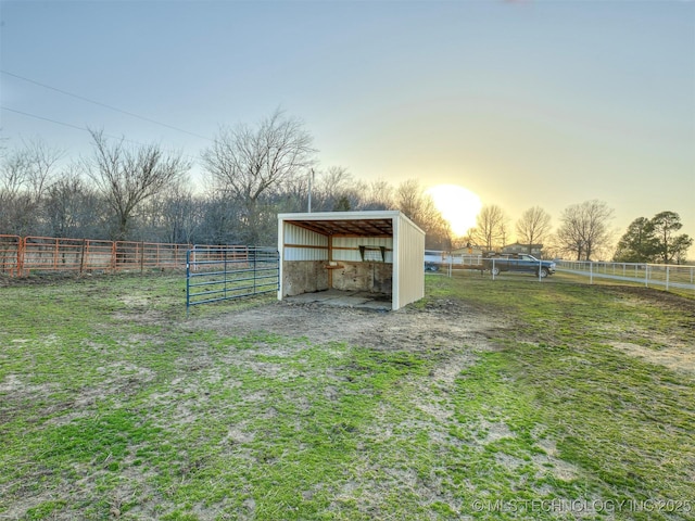 yard at dusk featuring an outbuilding, a rural view, an exterior structure, and fence