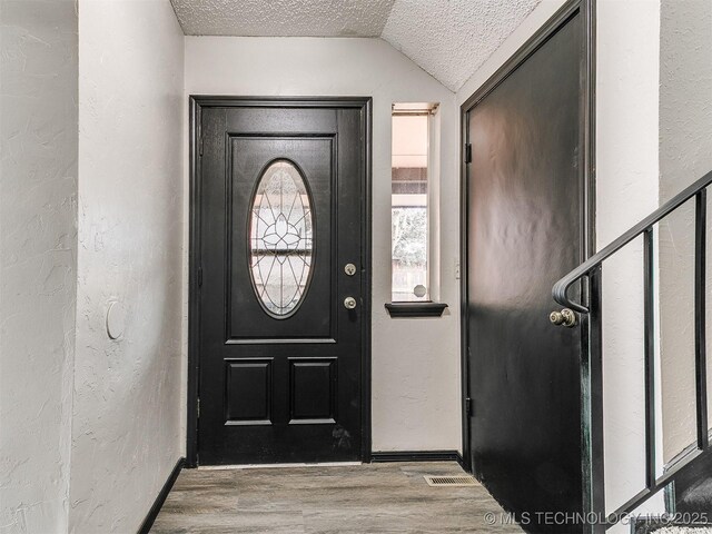 entrance foyer featuring vaulted ceiling, a textured ceiling, a textured wall, and wood finished floors