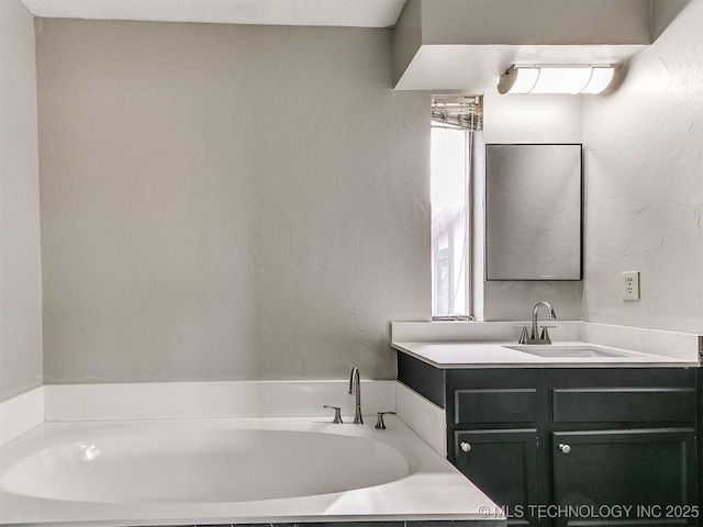 bathroom with a garden tub, vanity, and a textured wall