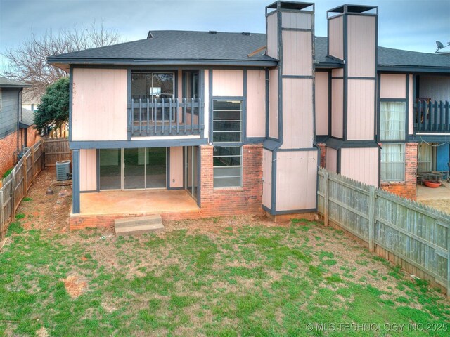 rear view of property featuring a yard, a fenced backyard, central AC, a chimney, and a shingled roof