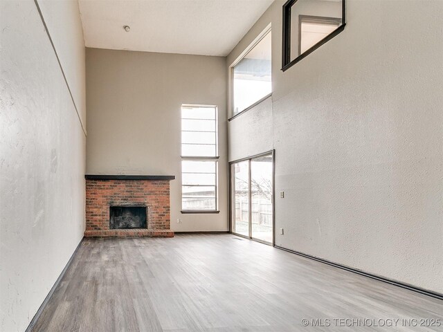 unfurnished living room with a textured wall, a fireplace, a towering ceiling, and wood finished floors