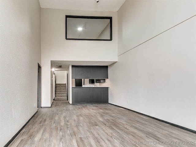 unfurnished living room featuring stairway, baseboards, a high ceiling, and wood finished floors