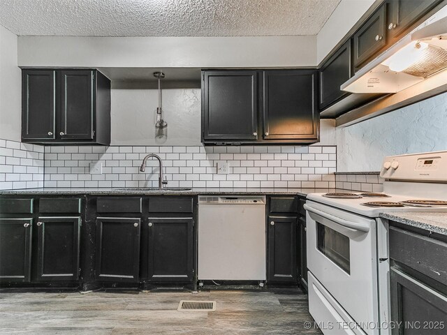 kitchen featuring white appliances, dark cabinets, under cabinet range hood, and a sink