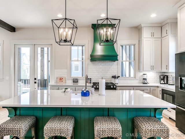 kitchen featuring black appliances, white cabinetry, light countertops, decorative backsplash, and a chandelier