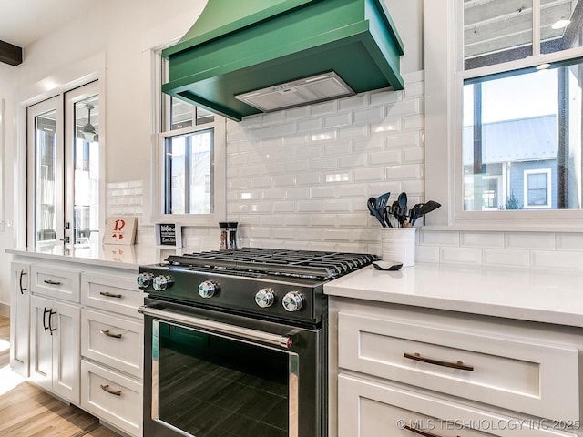 kitchen featuring tasteful backsplash, white cabinetry, exhaust hood, light countertops, and black range with gas cooktop