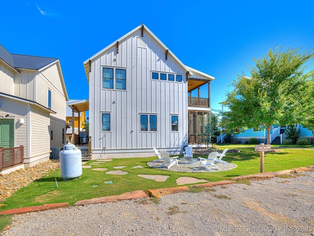 back of house featuring a balcony, a lawn, board and batten siding, and an outdoor fire pit