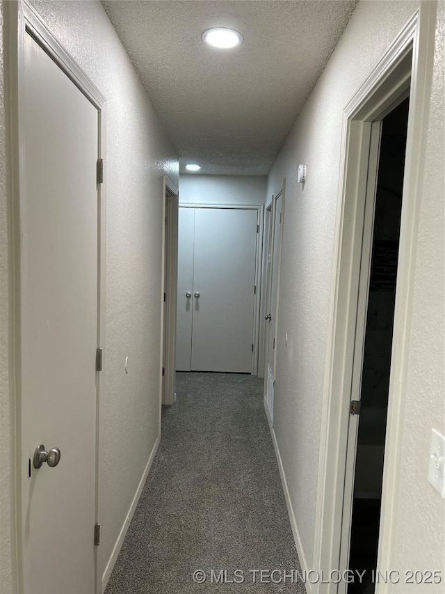 hall with baseboards, a textured ceiling, carpet, and a textured wall