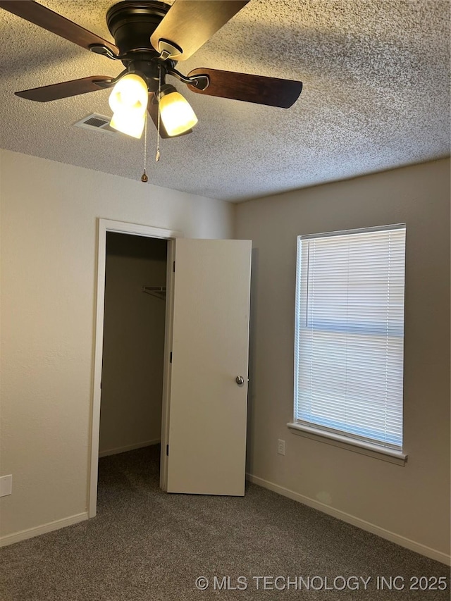 unfurnished bedroom with carpet, baseboards, ceiling fan, a textured ceiling, and a walk in closet