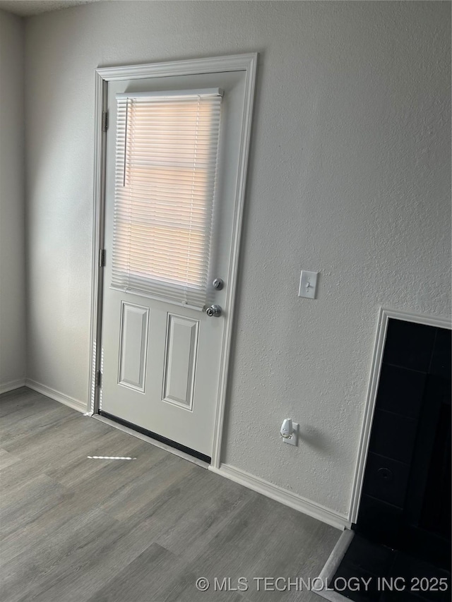 doorway to outside with a textured wall, baseboards, and wood finished floors