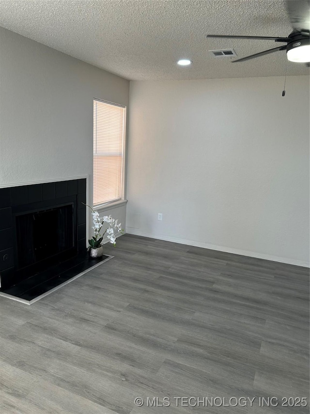 unfurnished living room with visible vents, a textured ceiling, wood finished floors, ceiling fan, and a tile fireplace