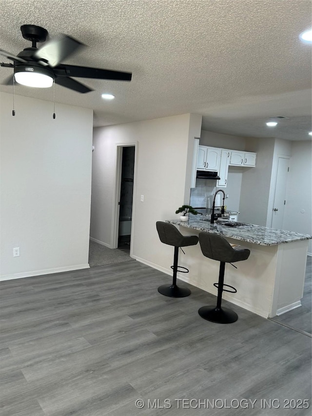 kitchen featuring a ceiling fan, a sink, dark wood finished floors, white cabinetry, and a peninsula