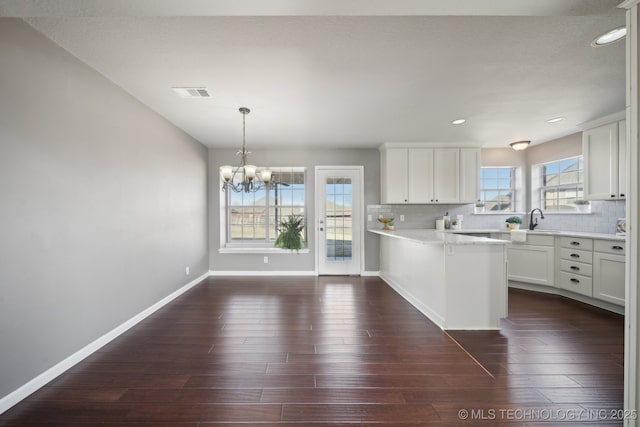 kitchen featuring visible vents, tasteful backsplash, an inviting chandelier, a peninsula, and dark wood-style flooring