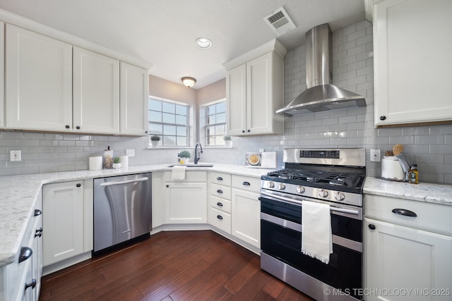 kitchen featuring visible vents, dark wood finished floors, stainless steel appliances, wall chimney exhaust hood, and white cabinets