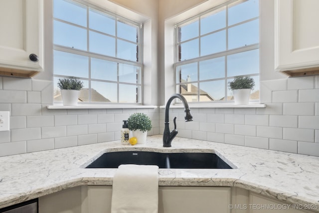 interior space featuring a sink, light stone countertops, tasteful backsplash, and white cabinets