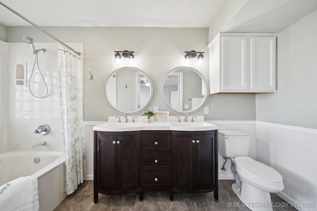 full bathroom with a sink, shower / bathtub combination with curtain, toilet, and wainscoting