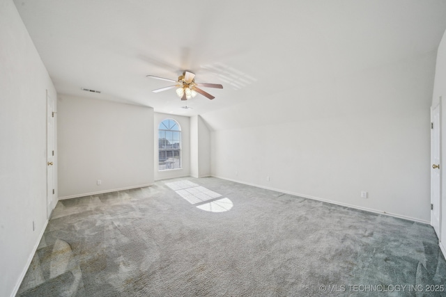 carpeted empty room featuring lofted ceiling, a ceiling fan, visible vents, and baseboards