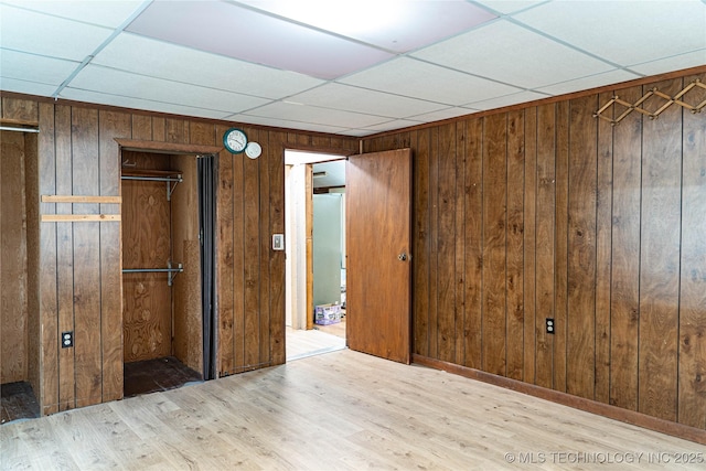 unfurnished bedroom featuring a closet, a paneled ceiling, wood finished floors, and wood walls