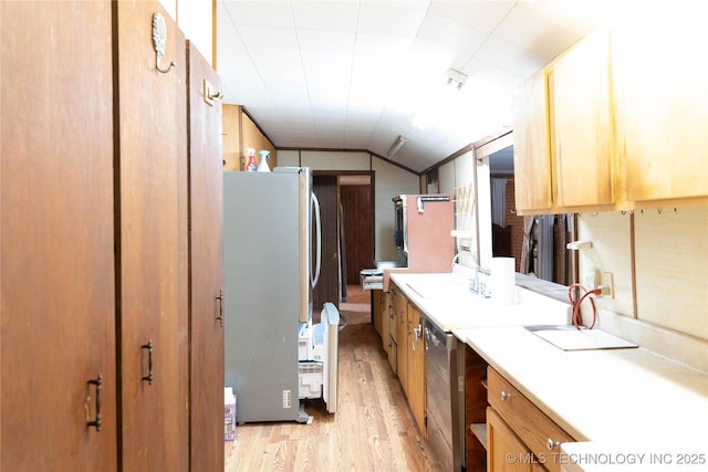 kitchen with a sink, stainless steel appliances, light wood-style floors, light countertops, and vaulted ceiling