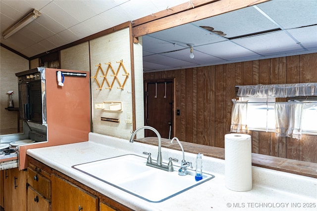 kitchen featuring light countertops, wooden walls, brown cabinets, and a sink