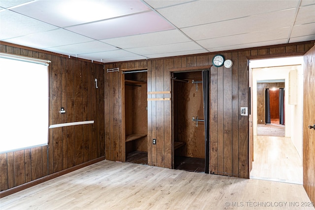 unfurnished bedroom with a drop ceiling, wood finished floors, and wood walls