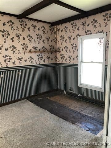 spare room featuring wallpapered walls, beam ceiling, and wainscoting