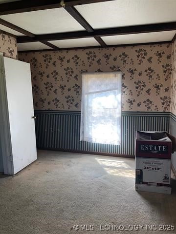 carpeted empty room featuring a wainscoted wall, beam ceiling, and wallpapered walls