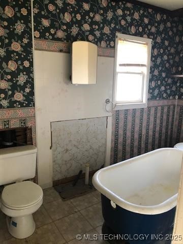 full bathroom with wallpapered walls, toilet, tile patterned flooring, and a freestanding bath