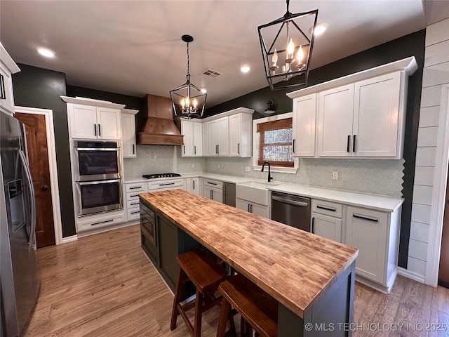 kitchen with an inviting chandelier, wood counters, appliances with stainless steel finishes, and custom exhaust hood