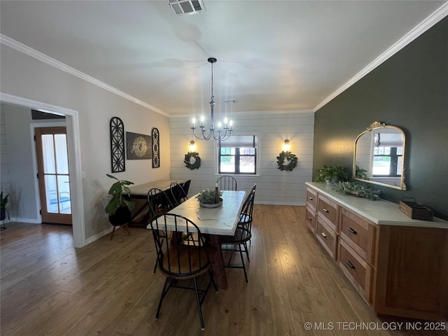 dining space with a notable chandelier, baseboards, wood finished floors, visible vents, and ornamental molding