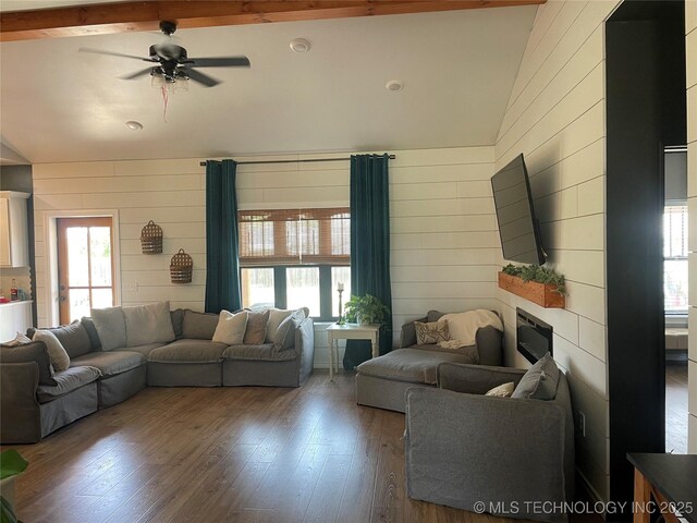 living room featuring vaulted ceiling with beams, a ceiling fan, wood walls, and hardwood / wood-style floors