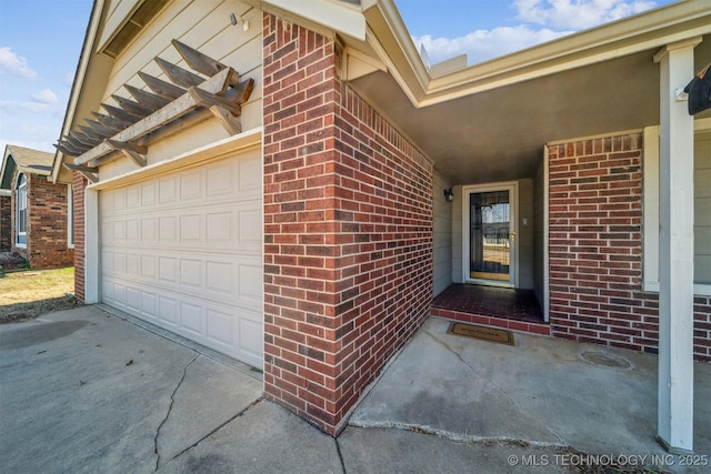 view of exterior entry featuring a garage, brick siding, and driveway