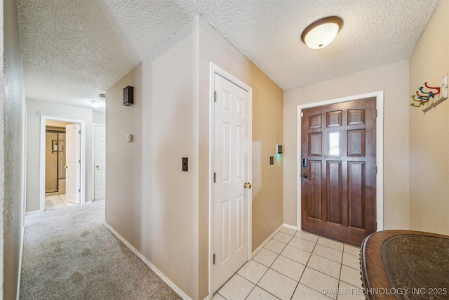 foyer entrance featuring light tile patterned floors, baseboards, light colored carpet, and a textured ceiling