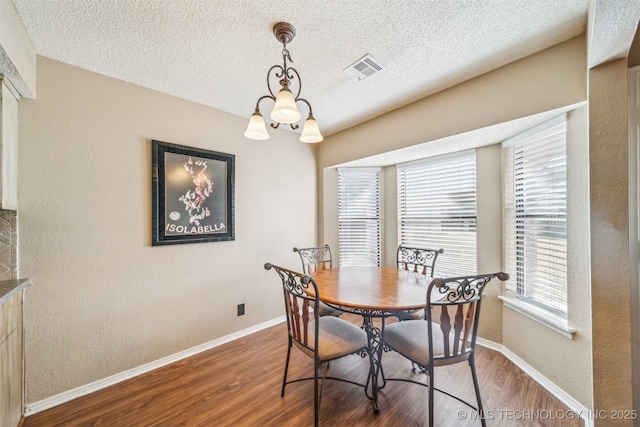 dining room with visible vents, baseboards, wood finished floors, a notable chandelier, and a textured ceiling