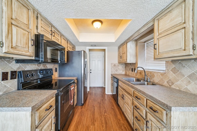 kitchen with black appliances, wood finished floors, a textured ceiling, a raised ceiling, and a sink