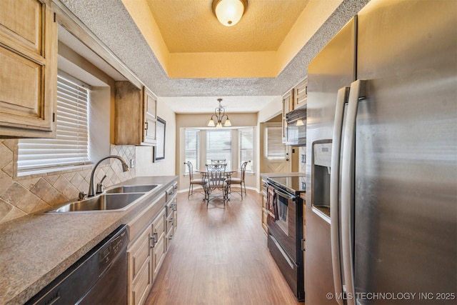 kitchen featuring black appliances, a sink, tasteful backsplash, wood finished floors, and a raised ceiling