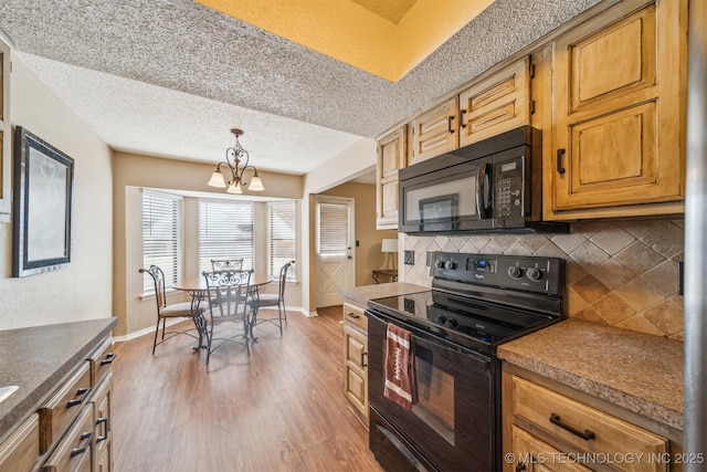 kitchen featuring black appliances, tasteful backsplash, wood finished floors, an inviting chandelier, and baseboards