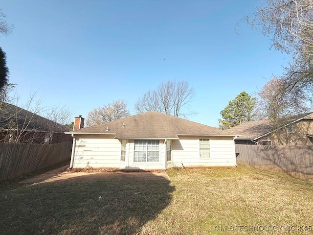 rear view of property with a shingled roof, a yard, fence, and a chimney