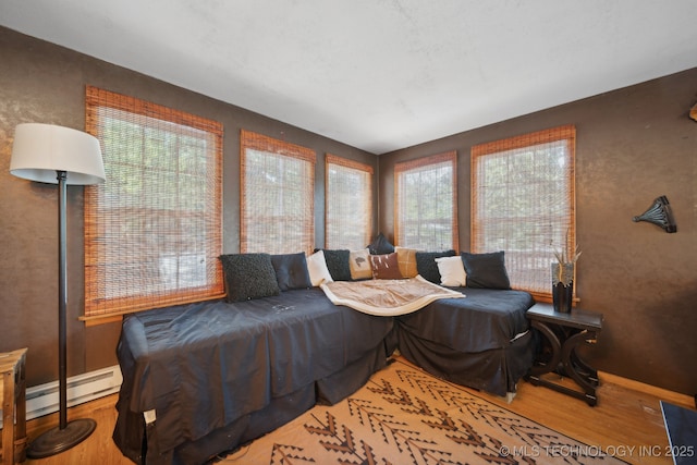 interior space with a baseboard heating unit, baseboards, and wood finished floors